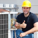 Air conditioning repairman working on a compressor and giving a thumbsup.